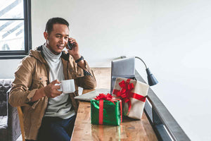 Man on the phone with a coffee cup by his work desk with holiday gifts