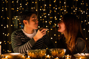 A couple enjoys a romantic dinner with the city lights behind them.