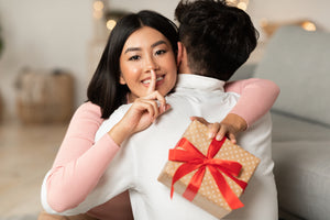 A woman hugs her boyfriend with a small gift in her hand.