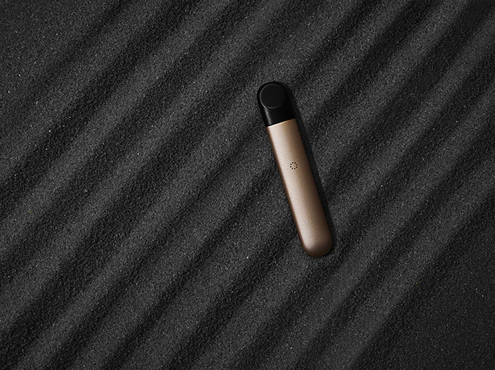 A gold RELX e-cig lies on black sand.