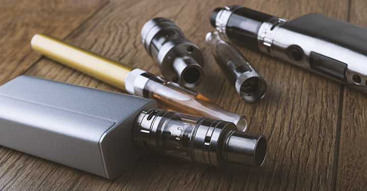 A pair of vapes and some atomizers lie on a wooden table.