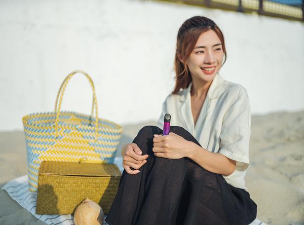  Asian woman relaxes by the beach with a RELX device in her hand.